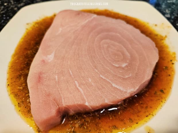 A piece of swordfish is placed in lemon herb marinade for flavoring.