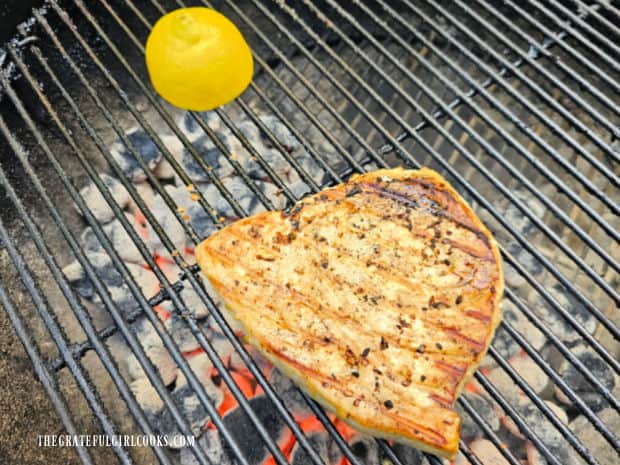 A swordfish steak and half a lemon cooking on the BBQ grill over hot coals.