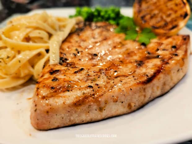 A piece of grilled lemon herb swordfish on a white plate with pasta.