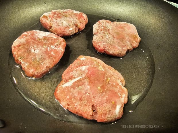 Four frozen ground pork sausage patties are cooked in water in skillet.