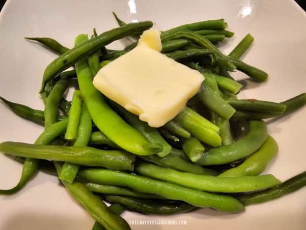 Hot green beans are transferred to serving bowl, then topped with butter.