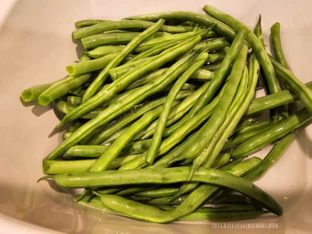 Fresh green beans are microwaved in a bowl with water.