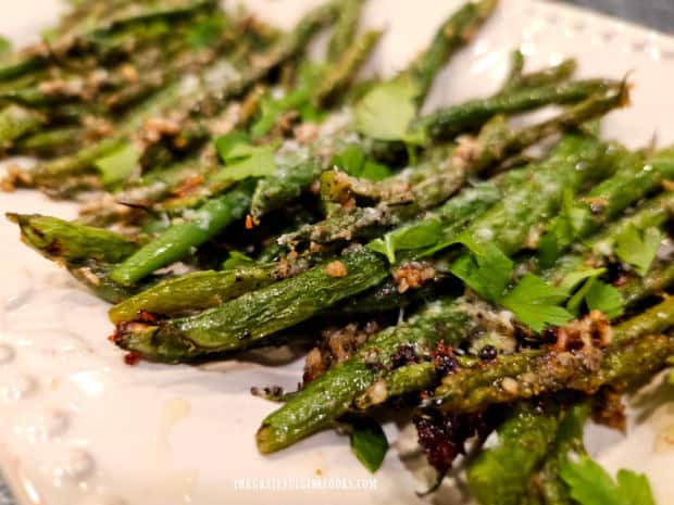 A platter of Parmesan Garlic Green Beans is topped with fresh, chopped parsley.