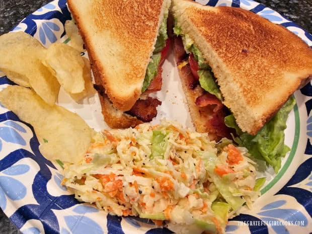 The classic creamy coleslaw on a paper plate, served with a sandwich and potato chips.