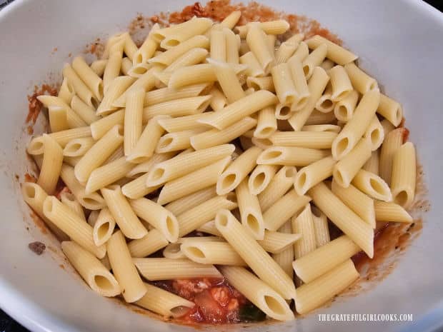 Drained and cooked penne pasta is added to the meat mixture in bowl.