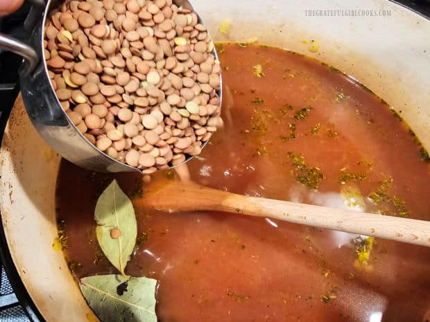 Brown lentils and two bay leaves are added to the minestrone soup in the pot.