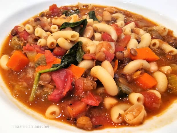 A white bowl, filled with easy lentil minestrone soup and served.