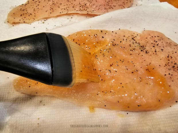 A pastry brush is used to coat both sides of each lightly seasoned chicken breast.